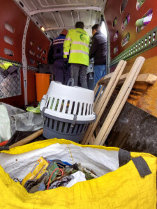 Interieur van een busje met afval op de voorgrond en drie mannen in de achtergrond, van links naar rechts een handhaver, RAD-medewerker en wethouder Robin Heij van gemeente Hoeksche Waard.