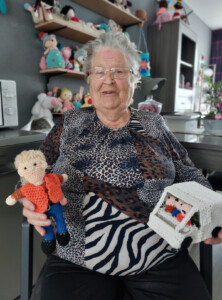 Mevrouw Spruijt met haar haakwerken. Op de achtergrond een wand vol andere haakwerken.