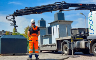 chauffeur van Waste Vision bedient kraan om containers te wisselen